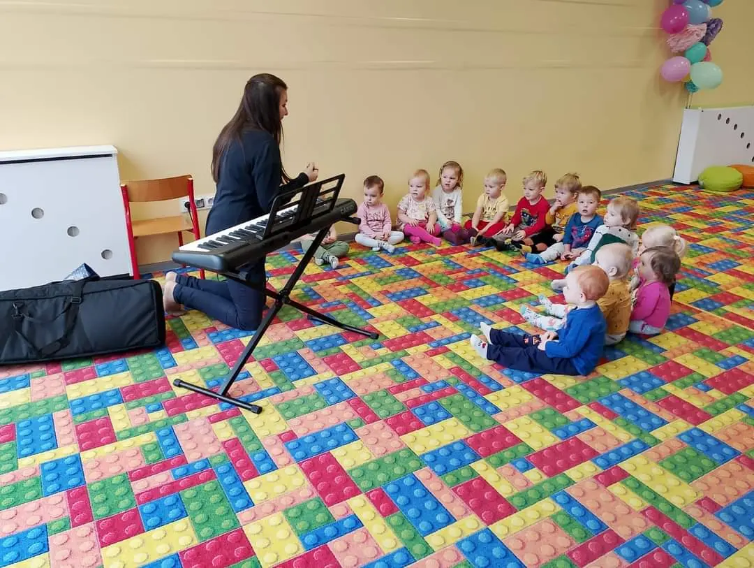 Skupione dzieci siedzą na podłodze, obok pani z keyboardem
