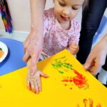 Dziecko odbijające ślady rąk na kartce żółtego papieru